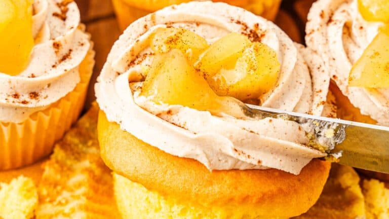 Cupcake with swirled frosting topped with apple pie filling and a sprinkle of cinnamon.