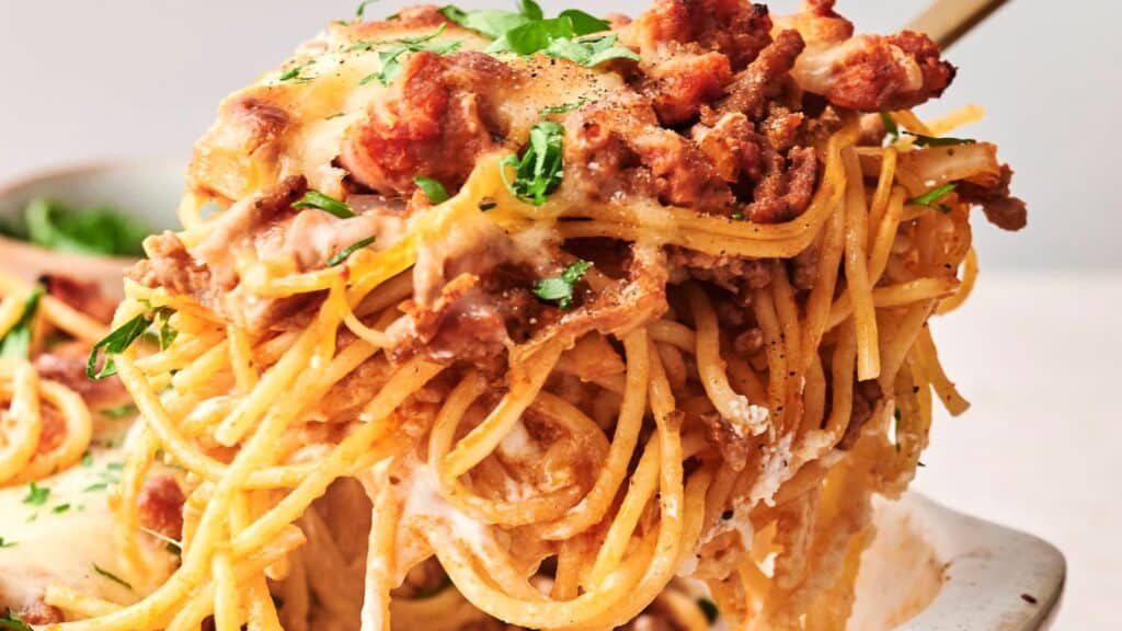 Close-up of a serving of baked spaghetti with melted cheese, meat, and garnished with parsley.