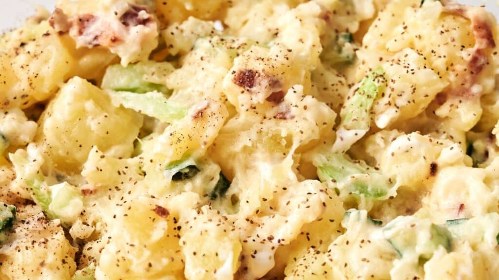 Close-up of potato salad with creamy dressing, pepper seasoning, chopped celery, and bacon bits.