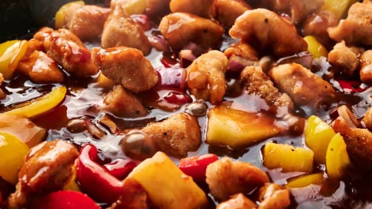 Close-up of sweet and sour chicken with bell peppers and pineapple chunks coated in sauce.