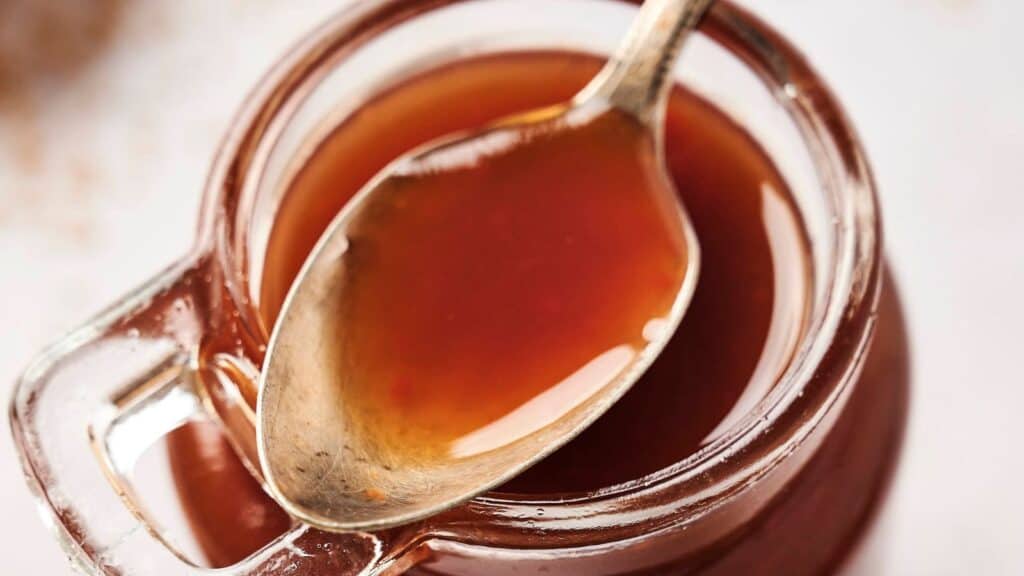 A close-up of a jar filled with brown sauce, with a spoon resting on the rim, partially submerged in the sauce.