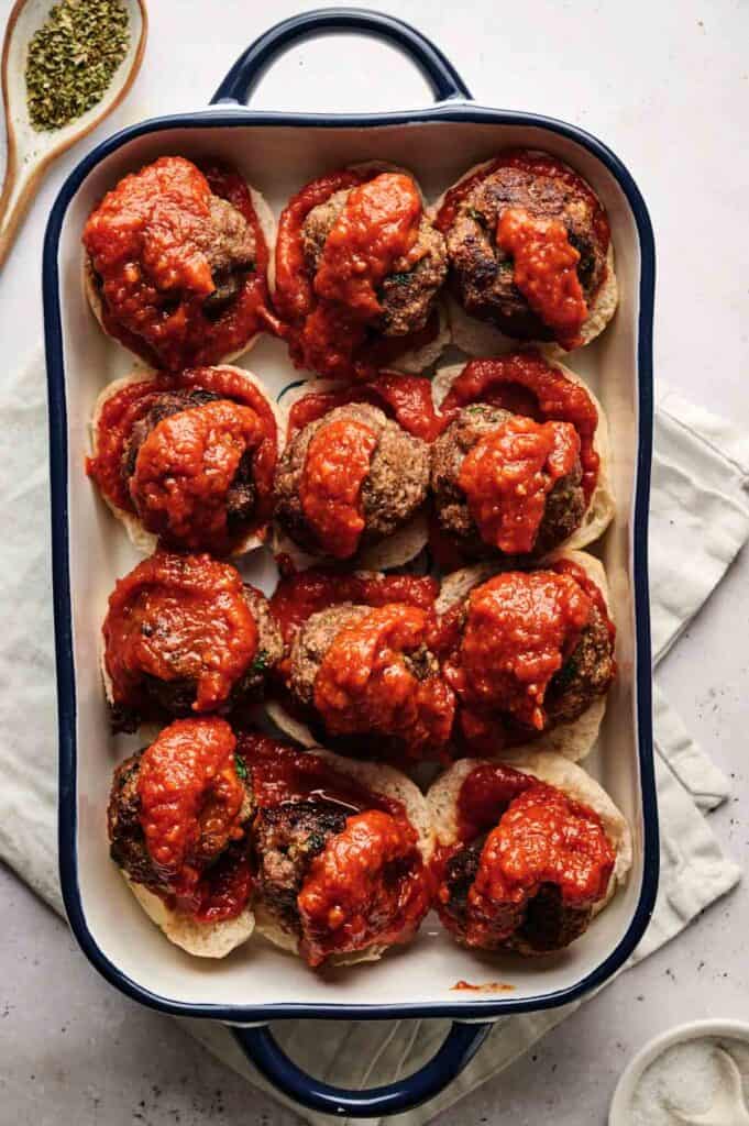 A baking dish filled with succulent meatball sliders, topped with rich tomato sauce, rests invitingly on a folded white napkin.