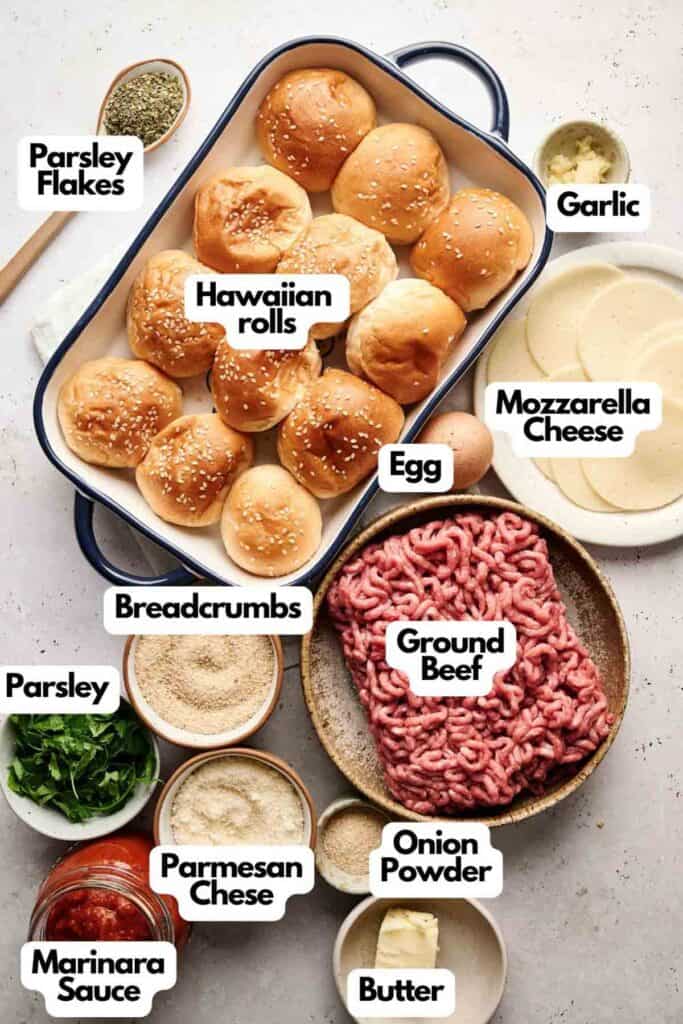 Top-down view of ingredients for delicious meatball sliders, featuring Hawaiian rolls, ground beef, mozzarella cheese, parmesan cheese, breadcrumbs, parsley flakes, eggs, onion powder, garlic butter, and marinara sauce.