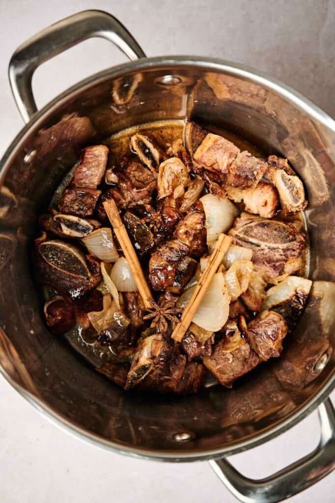 A pot containing browned meat, onions, star anise, and cinnamon sticks awaits its transformation into a rich broth reminiscent of tonkotsu ramen.