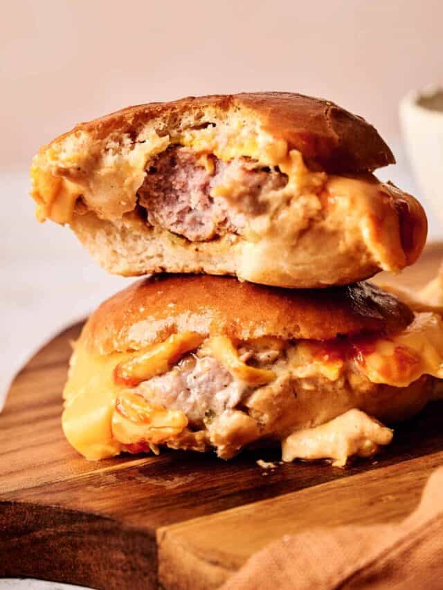 Two halves of a cheeseburger stacked on a wooden board, showcasing melted cheese and a beef patty.