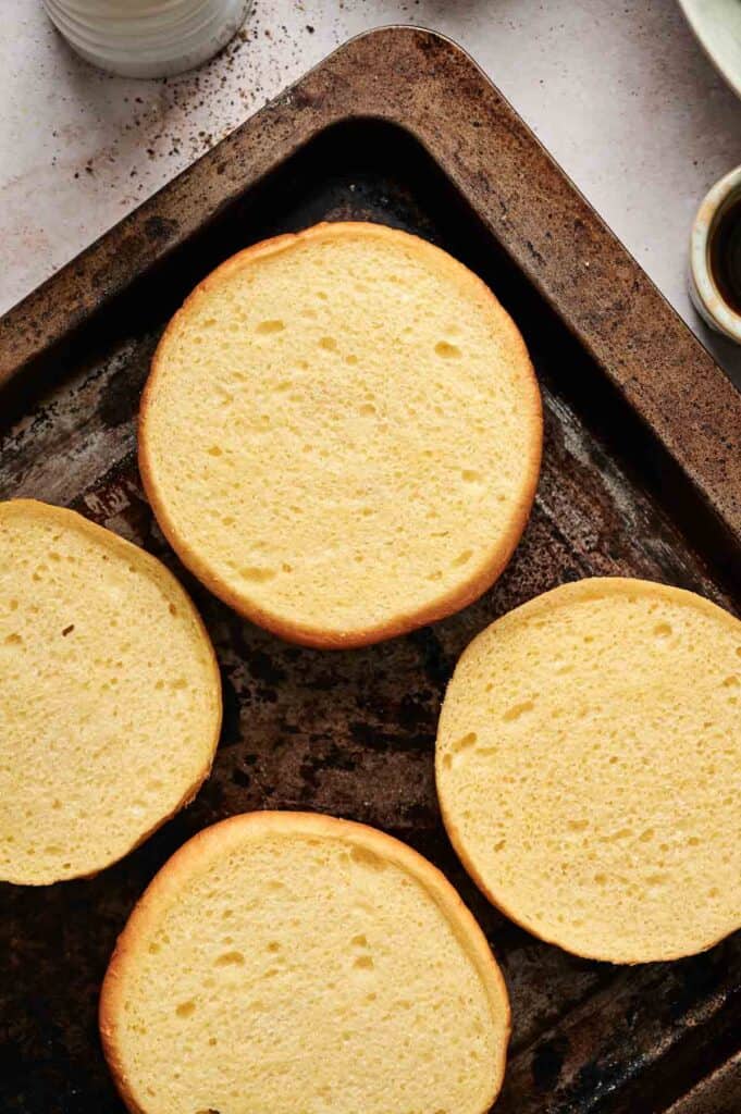 Four golden brown cheeseburger buns sliced in half on a baking sheet.