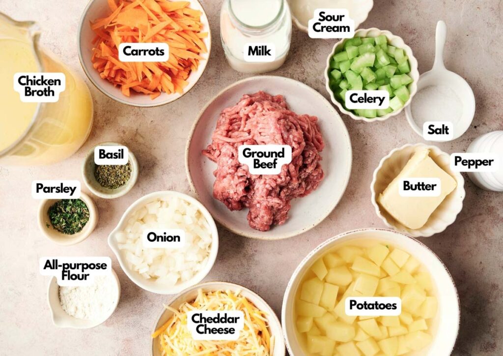 Overhead view of labeled ingredients in bowls, perfect for making cheeseburger soup, including ground beef, potatoes, cheddar cheese, onion, carrots, celery, chicken broth, sour cream, milk, spices, butter, flour, salt, and pepper.