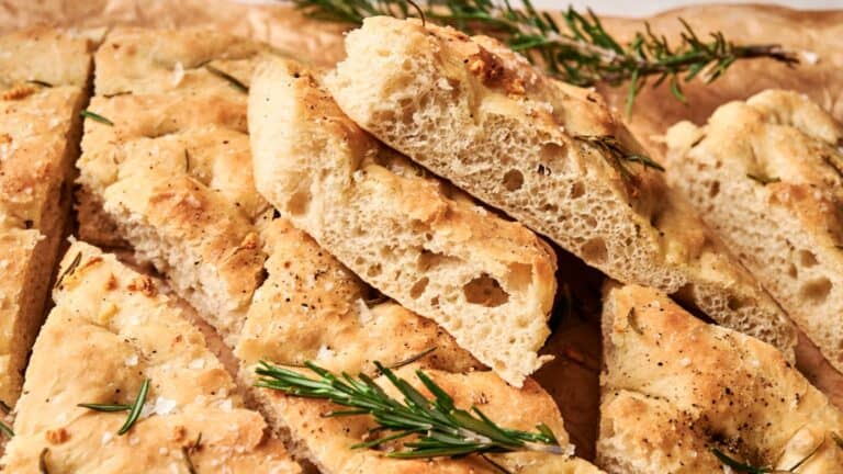 Slices of freshly baked focaccia bread topped with rosemary sprigs on parchment paper.