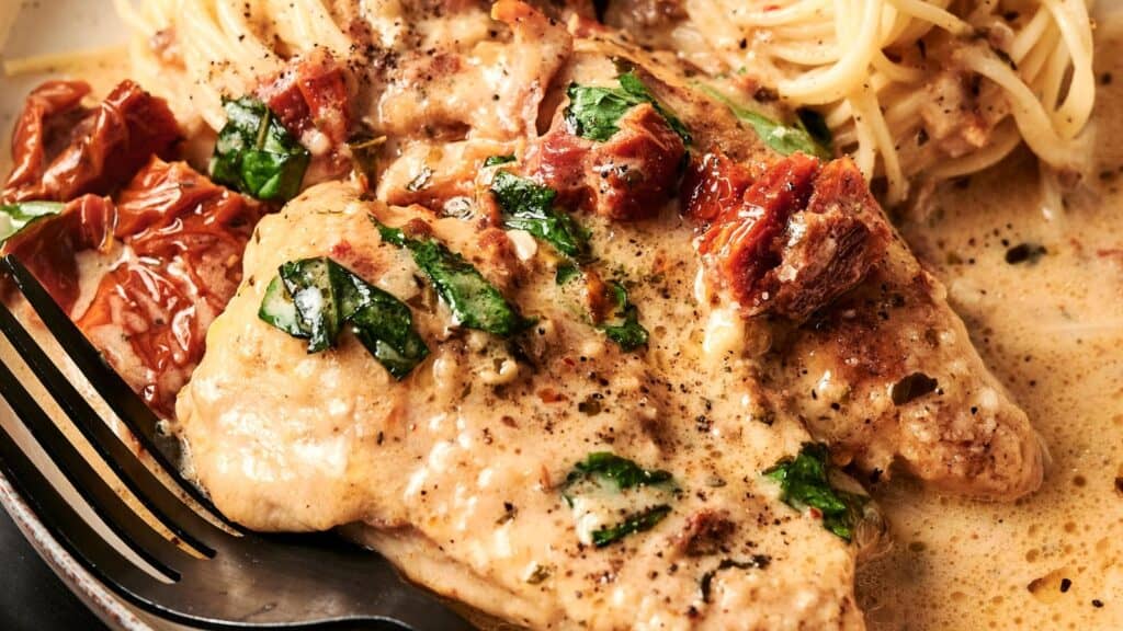 Creamy chicken breast topped with spinach and sun-dried tomatoes, served with spaghetti. A fork rests beside the dish.