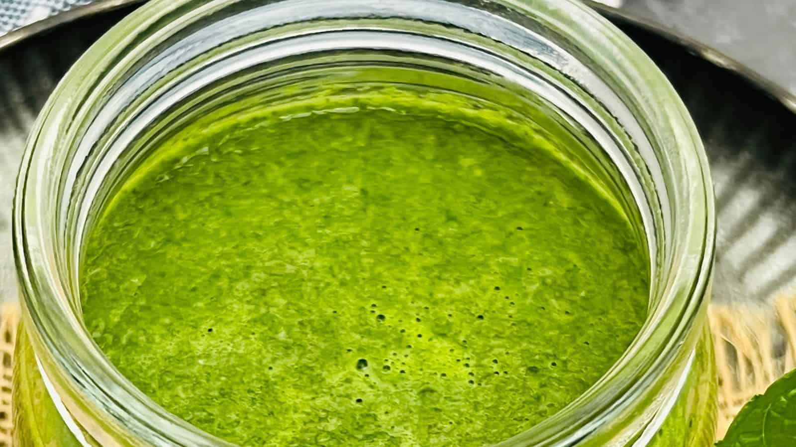 Top view of a glass jar containing bright green, freshly blended smoothie on a metallic tray.