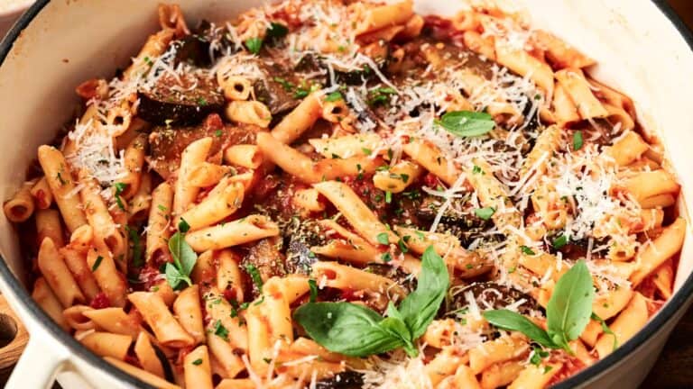 A pot of cooked pasta with tomato sauce, topped with grated cheese, fresh basil, and herbs.