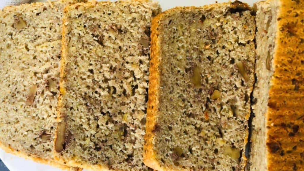 Close-up of sliced banana bread with visible nuts, showing a speckled, moist texture and a golden-brown crust.
