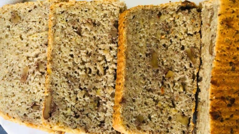 Close-up of sliced banana bread with visible nuts, showing a speckled, moist texture and a golden-brown crust.