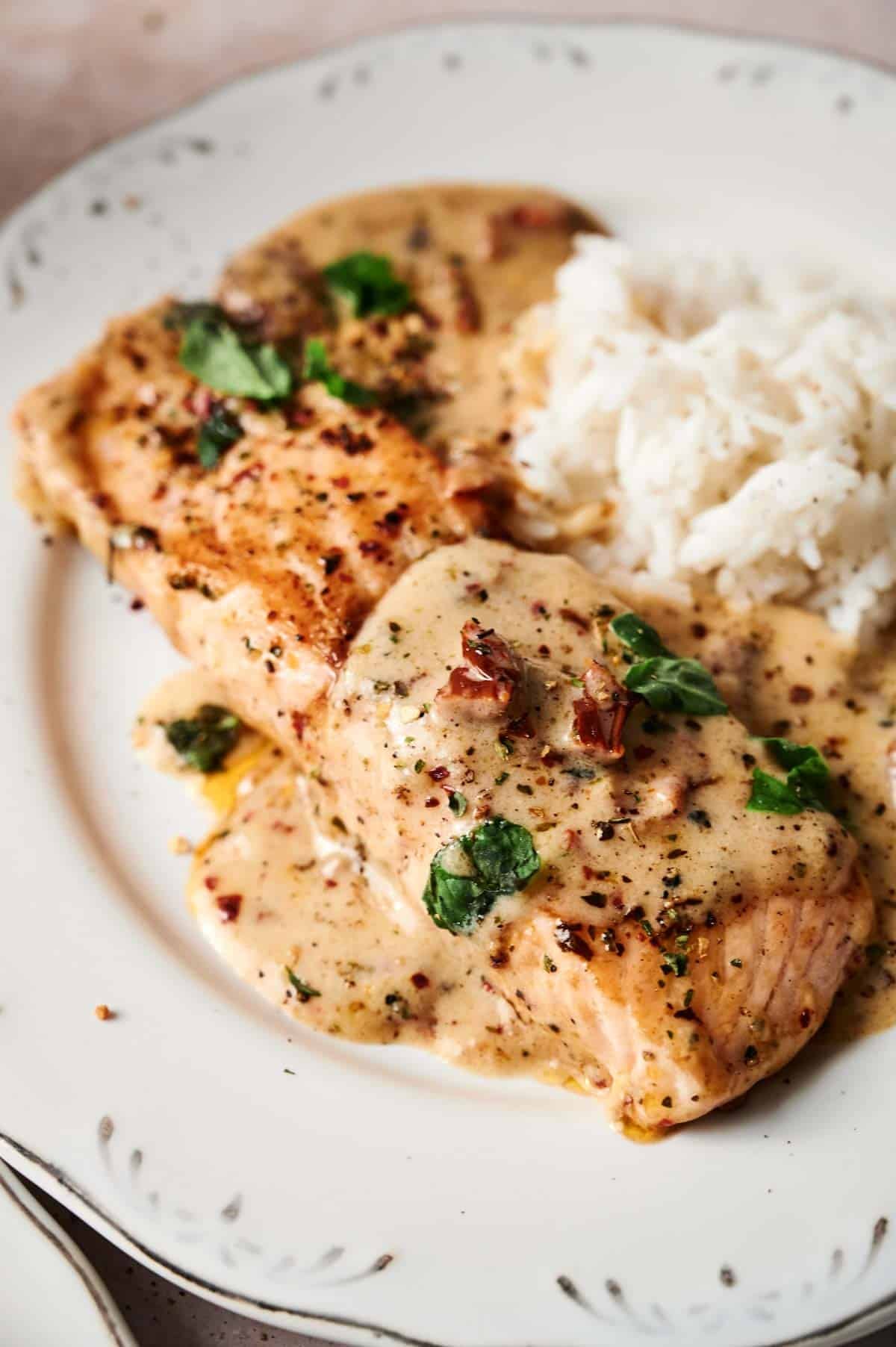 Plate with creamy sauce-covered salmon garnished with herbs and served alongside white rice.