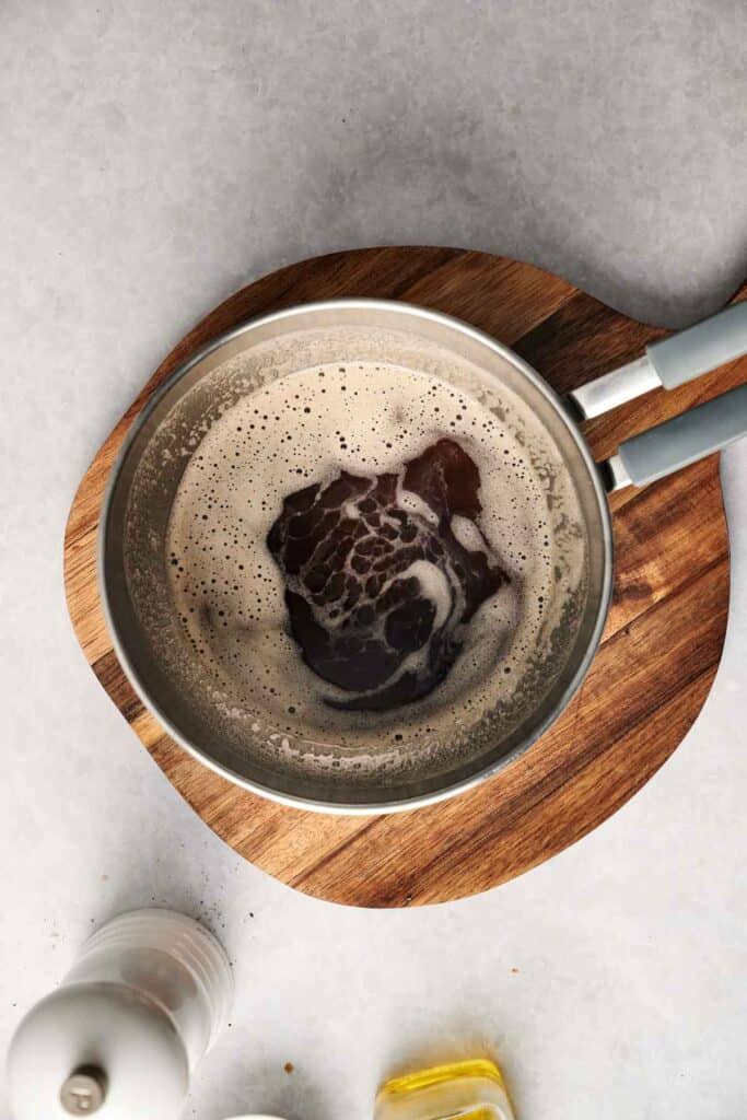 A coffee drink with frothy bubbles sits in a saucepan on a wooden board, resembling the creamy texture of mashed potatoes when viewed from above.