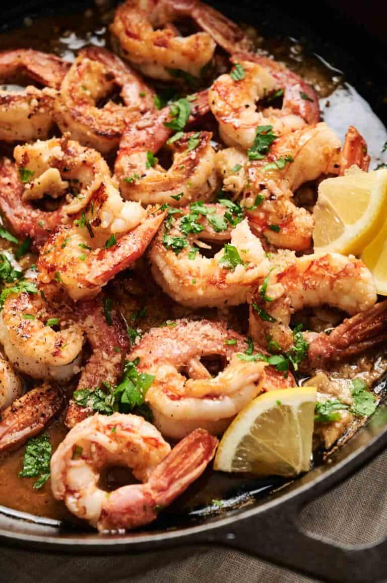 Shrimp scampi cooked in garlic butter sauce, garnished with chopped parsley and lemon wedges in a skillet.