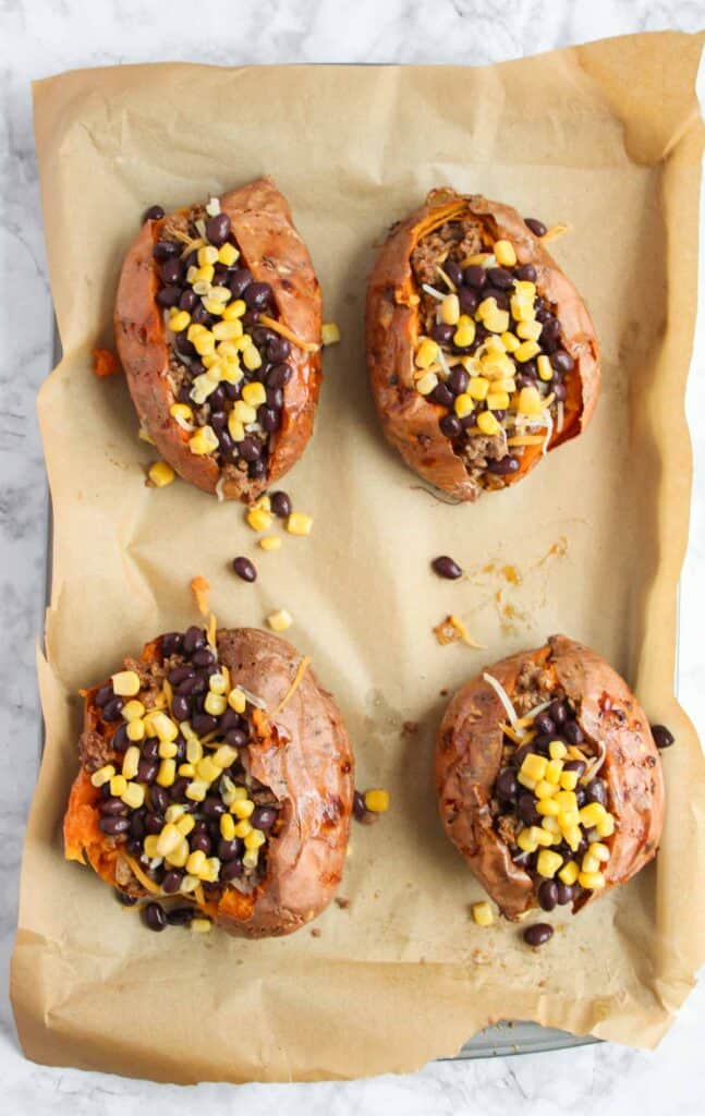 Four Southwest Stuffed Sweet Potatoes topped with black beans and corn sit invitingly on parchment paper.
