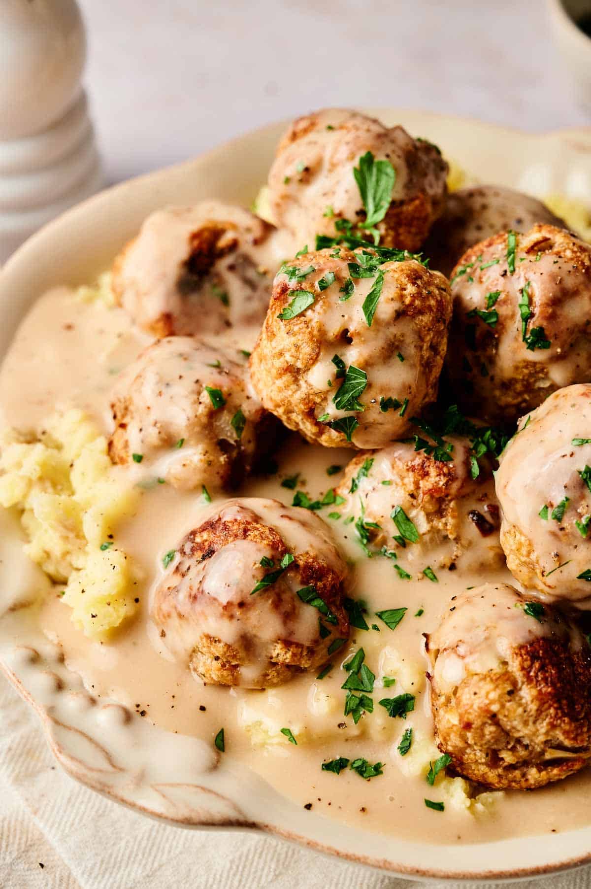 A plate of tender turkey meatballs covered in creamy gravy, garnished with chopped parsley, and served over fluffy mashed potatoes.