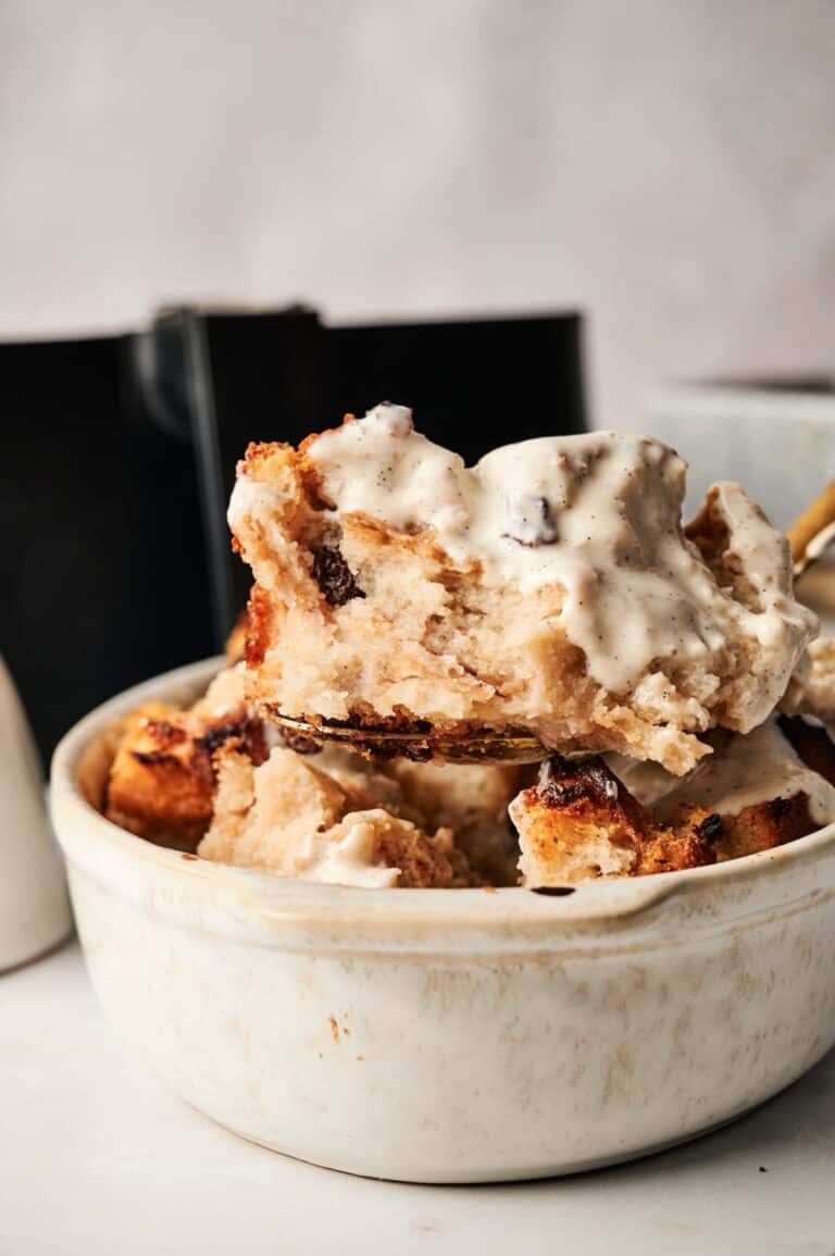 A bowl of air fryer bread pudding topped with a creamy sauce.