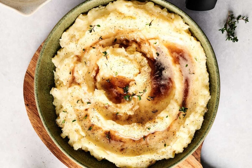 A bowl of Air Fryer Mashed Potatoes topped with brown gravy and sprinkled with black pepper and fresh thyme.