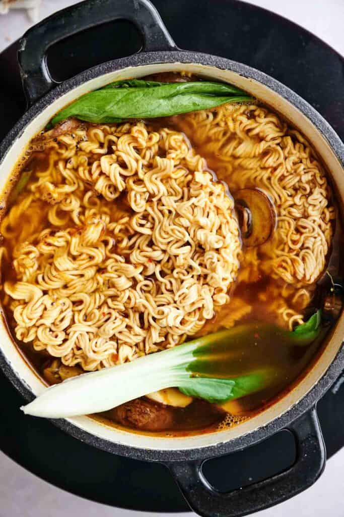 Pot of ramen noodles and pak choi in broth on a stovetop.