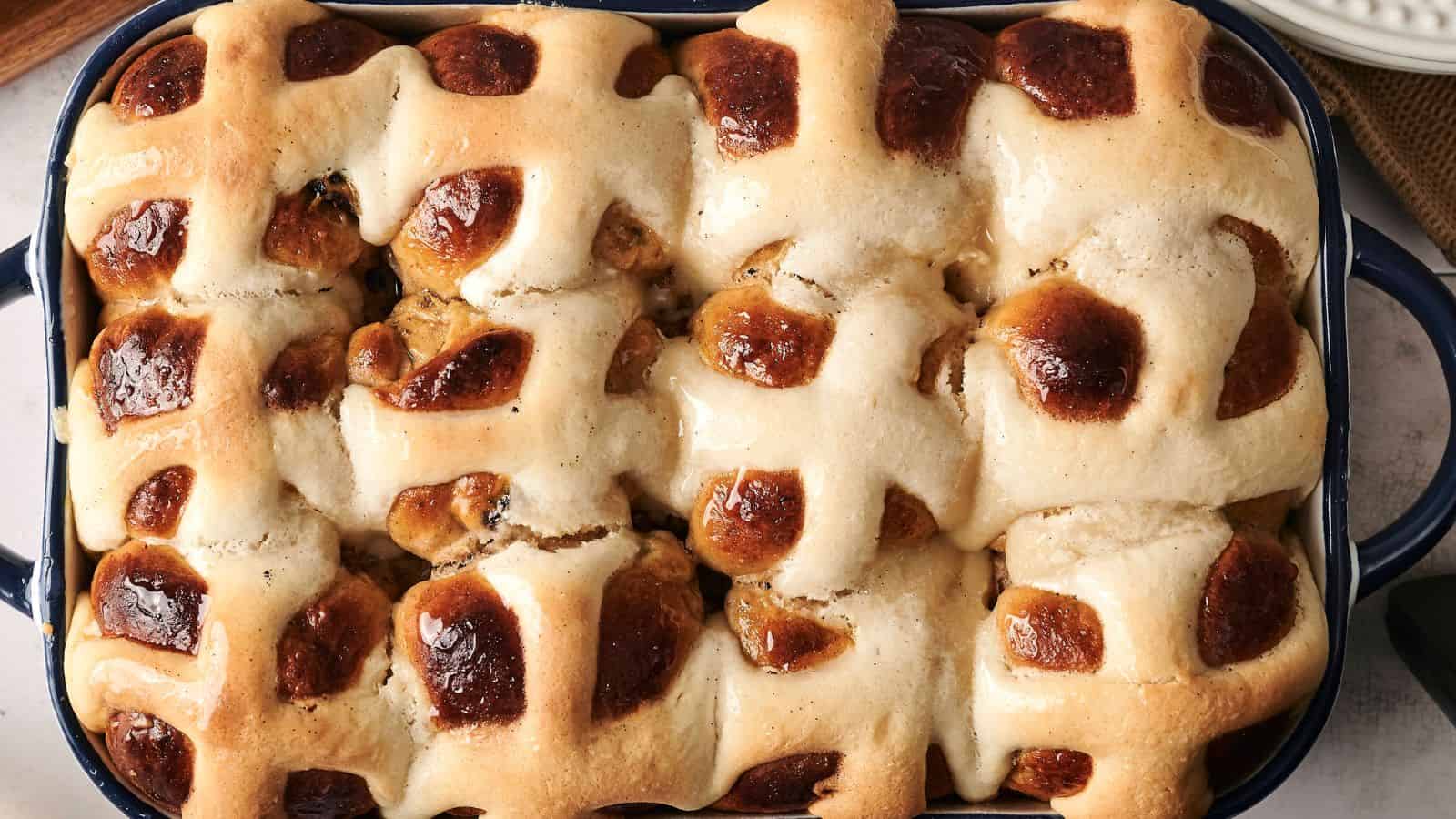A baking dish filled with freshly baked hot cross buns, featuring a golden-brown crust and white icing crosses on top.