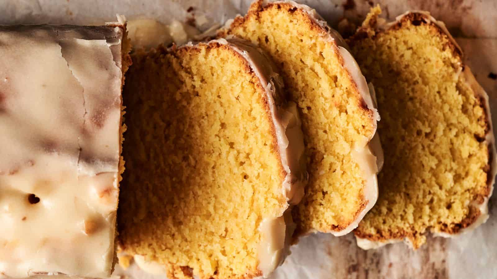 Sliced lemon drizzle cake on parchment paper, showing a moist crumb and glistening glaze.