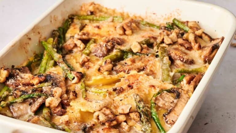 Baked casserole with asparagus, sliced mushrooms, and chunks of nuts topped with melted cheese in a white dish.