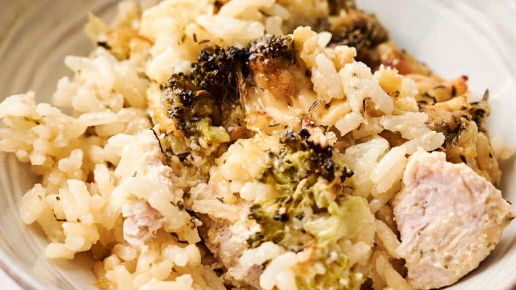 A bowl of cooked rice mixed with broccoli and pieces of chicken.