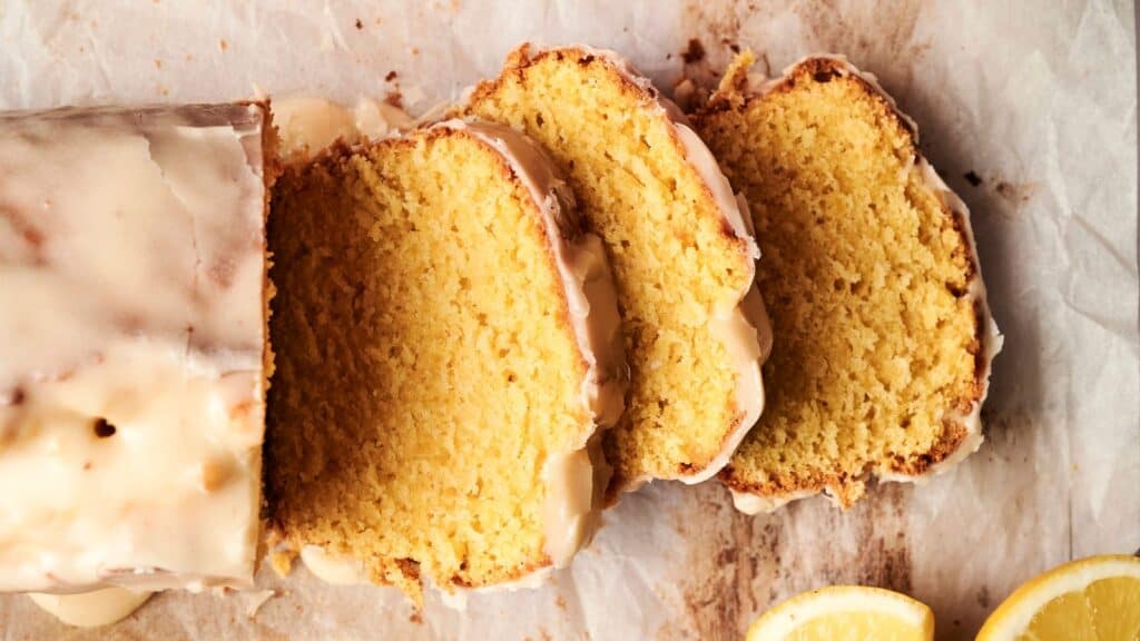 Sliced lemon loaf cake with glaze, arranged on parchment paper.