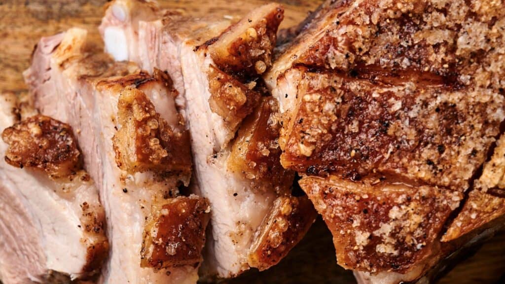 Sliced roasted pork with crispy skin on a wooden surface.