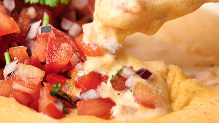 Close-up of creamy cheese dip being poured onto diced tomatoes and onions, garnished with cilantro.