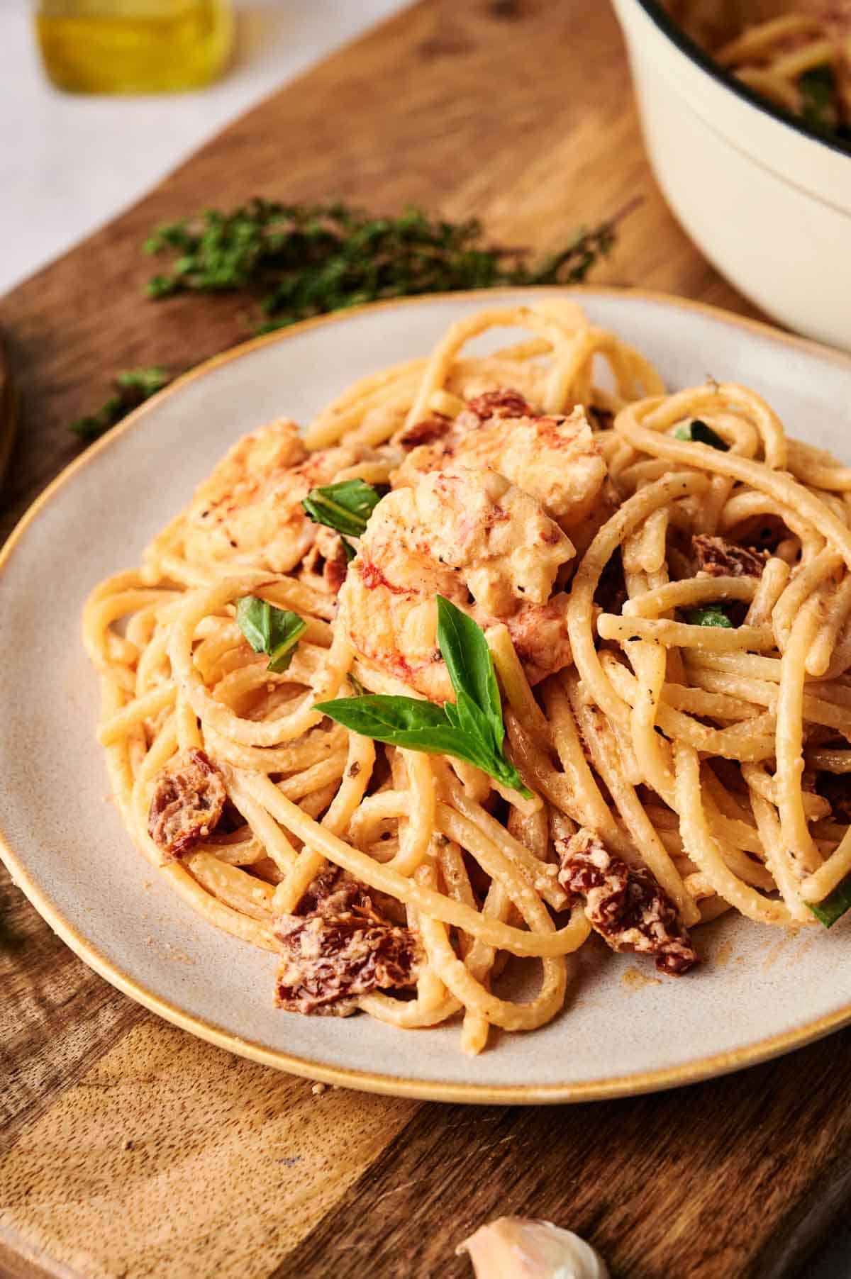 A plate of marry me shrimp pasta with creamy sauce, sun-dried tomatoes, and fresh basil rests on a wooden surface.