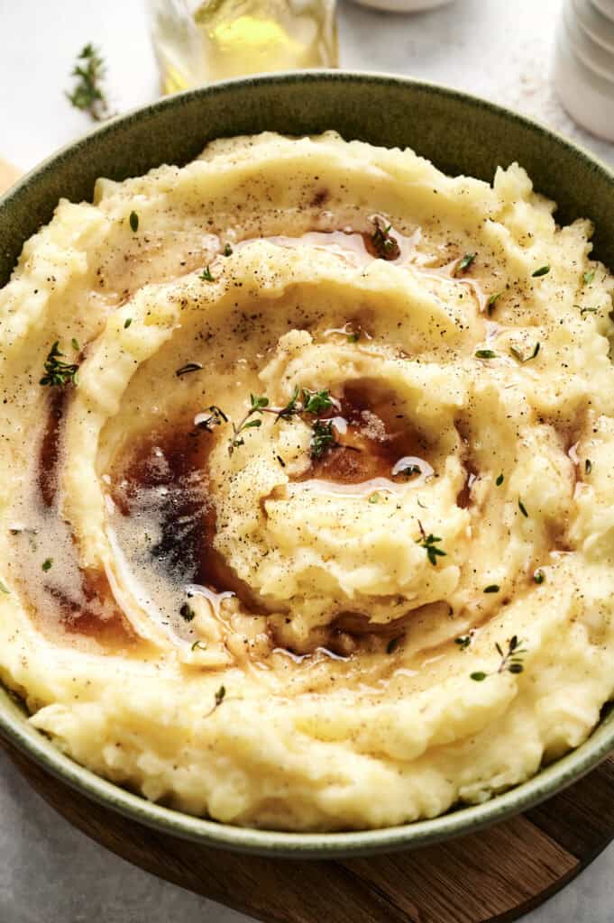 A bowl of creamy Air Fryer mashed potatoes topped with melted butter, black pepper, and fresh thyme.