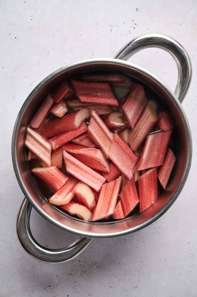 A pot teeming with chopped rhubarb pieces, destined for a delightful rhubarb crisp, sits submerged in water on a light-colored surface.