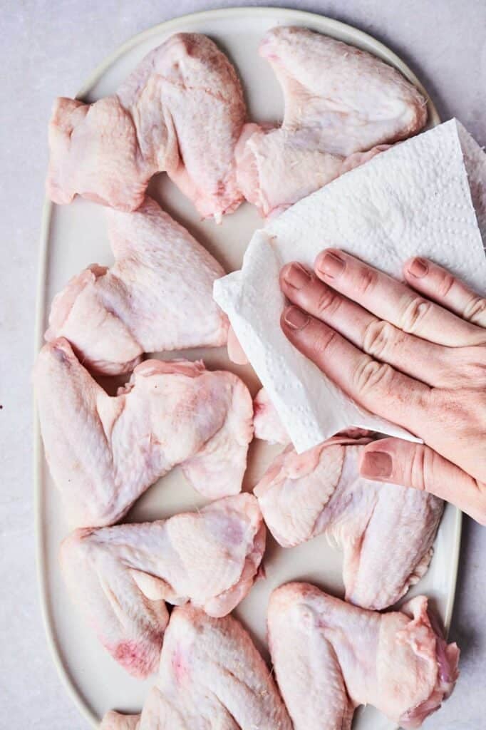 A person gently pats Wingstop Louisiana Rub Wings with a paper towel on a white plate, ensuring each piece is ready for perfection.