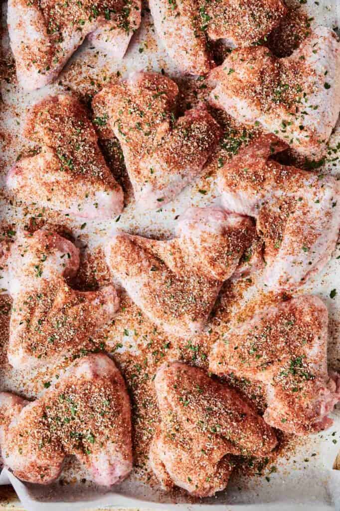 Raw chicken wings, reminiscent of Wingstop's Louisiana Rub Wings, are coated in a flavorful spice blend with herbs and neatly arranged on a parchment-lined baking sheet.