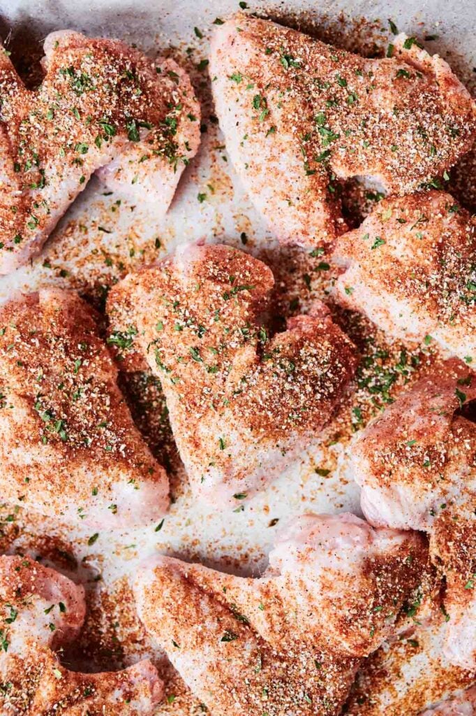 Raw Wingstop Louisiana Rub style chicken wings seasoned with spices and herbs on a baking sheet.