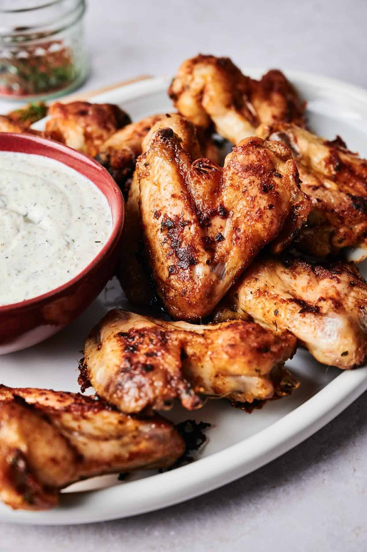 Grilled chicken wings on a white plate with a bowl of creamy dipping sauce, featuring the bold flavors of Wingstop's Louisiana Rub Wings.