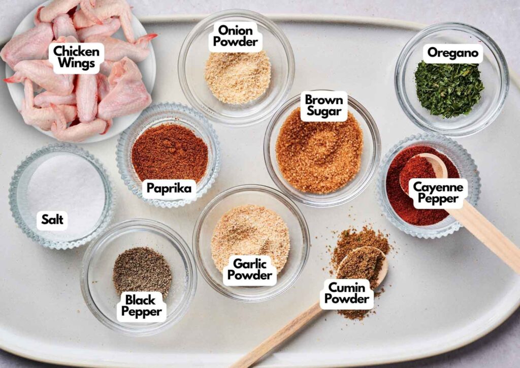 A tray displays raw chicken wings, salt, black pepper, paprika, onion powder, garlic powder, brown sugar, cumin powder, cayenne pepper, and oregano in labeled bowls—perfect for making Wingstop Louisiana Rub Wings.