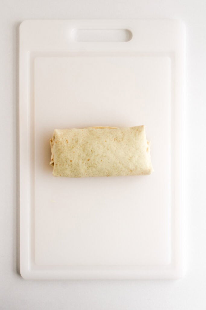 A single Beef and Potato Burrito Taco Bell Copycat is wrapped and placed in the center of a white cutting board.
