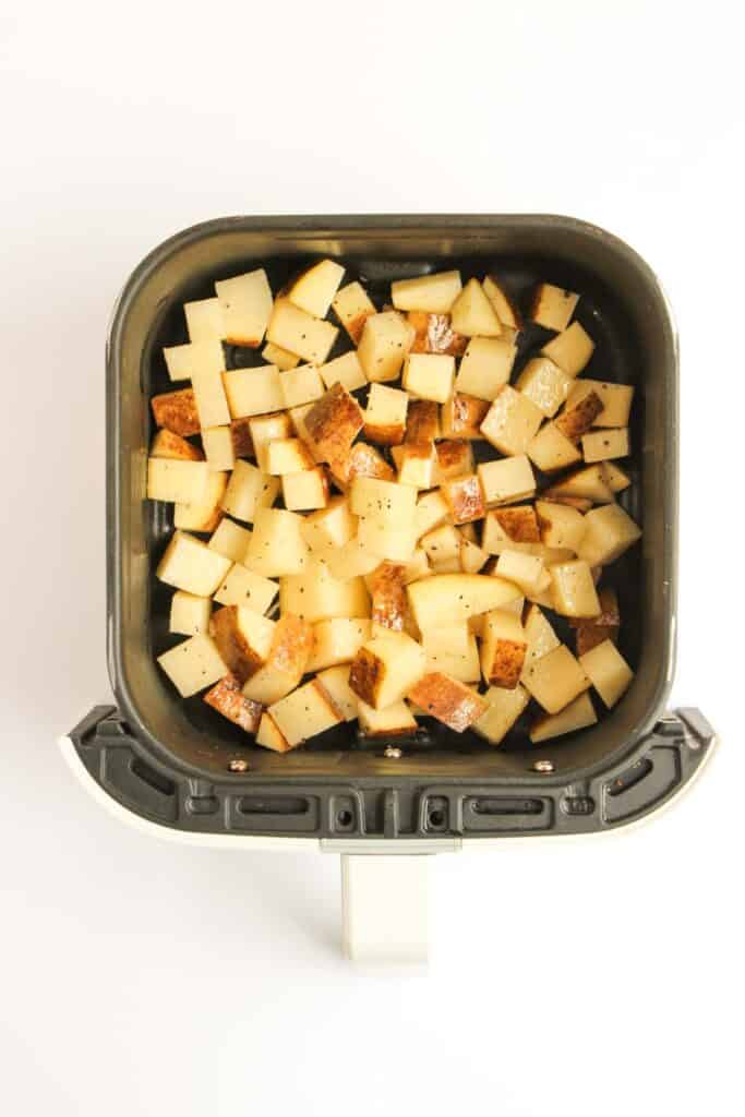 Diced potatoes with skins on are seasoned and arranged in a single layer inside an air fryer basket&mdash;perfect for making a Beef and Potato Burrito Taco Bell Copycat at home.