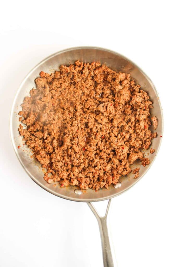 A stainless steel skillet filled with cooked and browned ground beef, just like the savory filling in a Beef and Potato Burrito Taco Bell Copycat, shown from above on a white background.