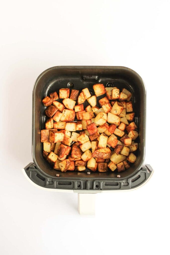 Diced, seasoned potatoes cooked in an air fryer basket for a delicious Beef and Potato Burrito Taco Bell Copycat, photographed from above on a white background.