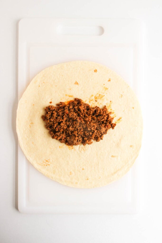 A Beef and Potato Burrito Taco Bell Copycat features a flour tortilla with seasoned ground beef filling, placed on a white cutting board.