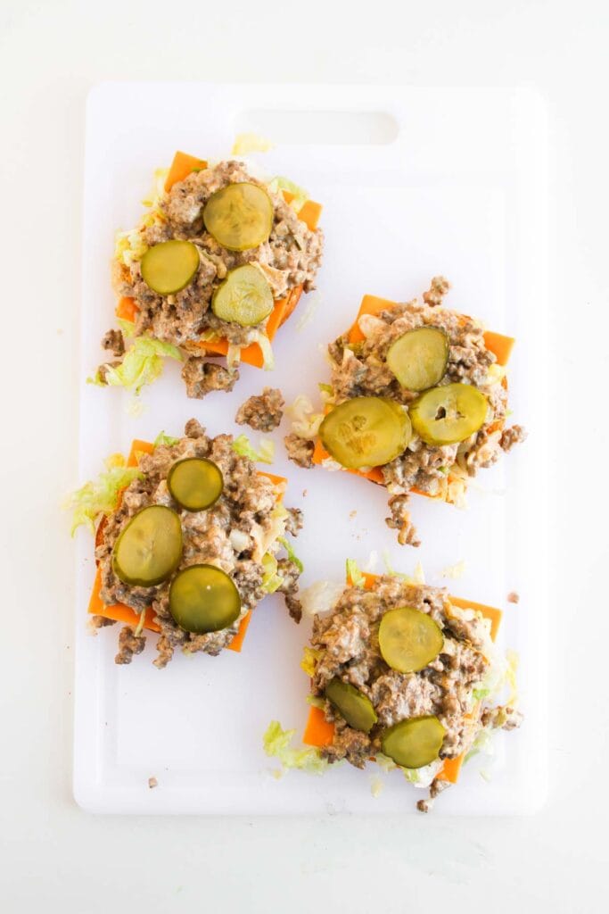 Four Big Mac Sloppy Joes lettuce and cheese stacks topped with ground meat mixture and pickle slices are arranged on a white cutting board.
