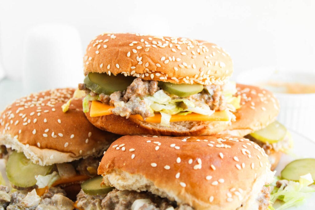 Three sesame seed hamburger buns filled with ground beef, cheddar cheese, pickles, lettuce, and signature sauce—just like classic Big Mac Sloppy Joes—stacked on a plate.