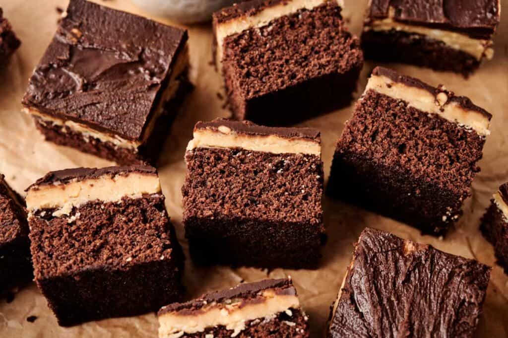 Several pieces of chocolate cake with a peanut butter filling layer are arranged on brown parchment paper, reminiscent of a decadent ice cream cake indulgence.