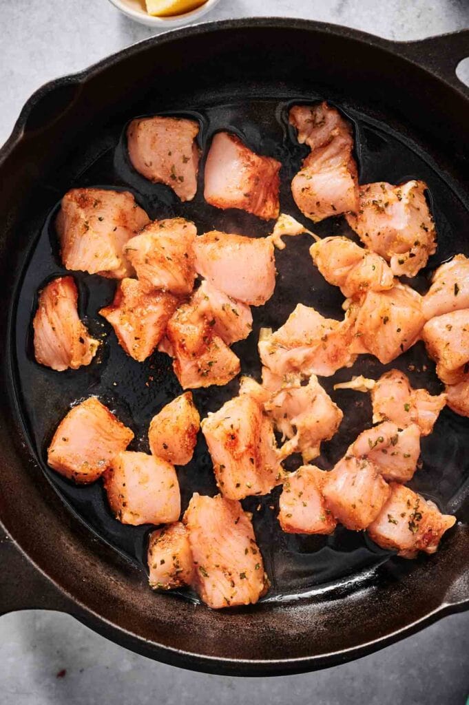 Chunks of seasoned chicken sizzle in a black skillet, ready to elevate your Chicken Caesar Pasta Salad with their savory flavor.