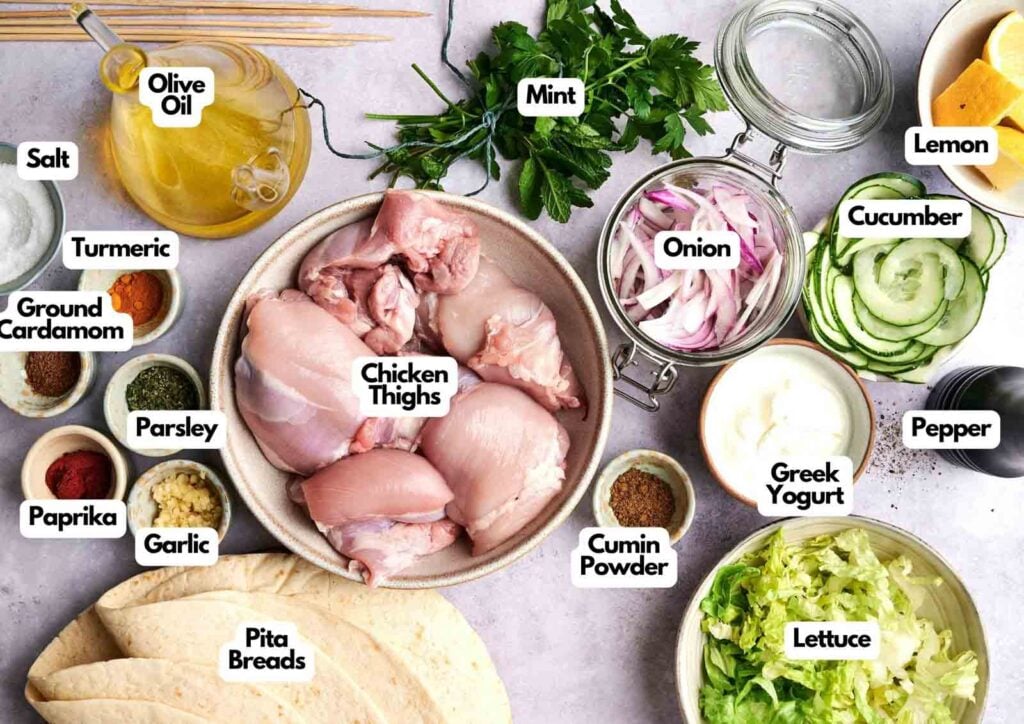 Chicken Shawarma ingredients are arranged on a table, featuring chicken thighs, spices, herbs, vegetables, Greek yogurt, pita bread, all clearly labeled for an easy Chicken Shawarma preparation.